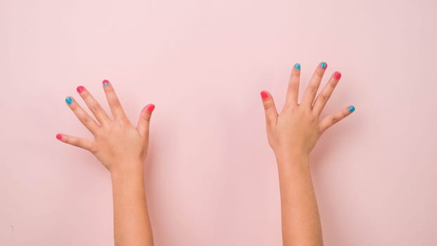 Close-up of raised child hand showing nail polish on pastel pink background in studio. Pack of Gestures movements and body language.