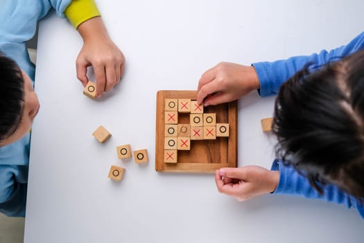 Little siblings playing wooden board game tic-tac-toe on table in living room. Family spending time together on weekend.