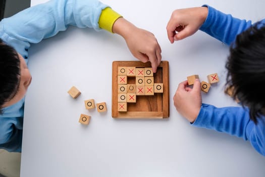 Little siblings playing wooden board game tic-tac-toe on table in living room. Family spending time together on weekend.