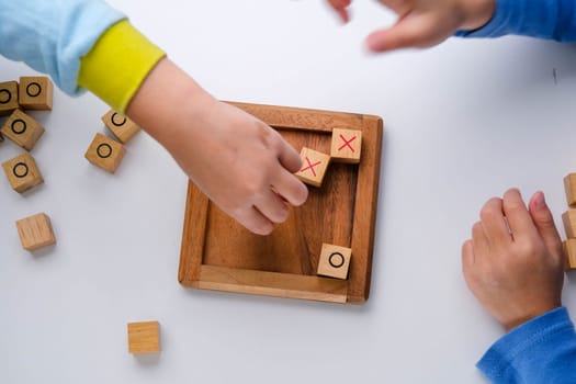 Little siblings playing wooden board game tic-tac-toe on table in living room. Family spending time together on weekend.