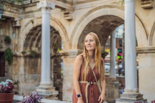 Happy female tourist traveler discover interesting places and popular attractions and walks in the old city of Antalya. Hadrian Kapisi turkey landmark city history. Popular tourist attraction - ancient Roman Hadrian Gate in old town Antalya, Turkey on a summer day. Turkiye.