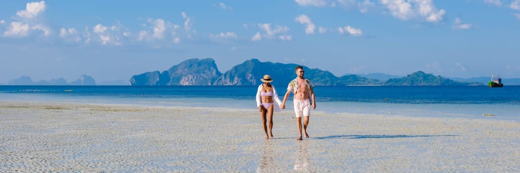 a couple of men and woman on the beach of Koh Kradan Island Thailand, men and women relaxing on the beach with a turqouse colored ocean on a sunny day