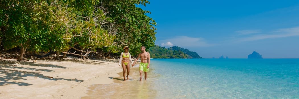 the backside of a couple of men and women sitting at the beach of Koh Kradan island in Thailand during vacation on a sunny day