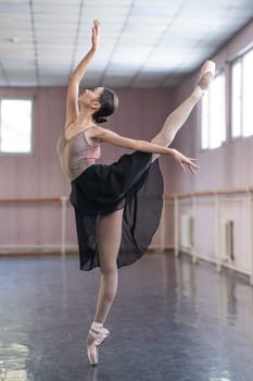 Graceful Asian ballerina in a beige bodysuit and black skirt is rehearsing in a dance class