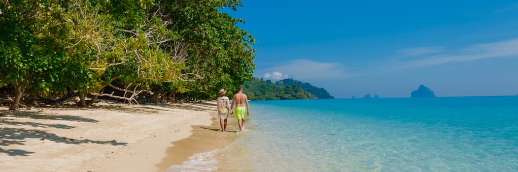 the backside of a couple of men and women sitting at the beach of Koh Kradan island in Thailand during vacation on a sunny day at holiday on the beach