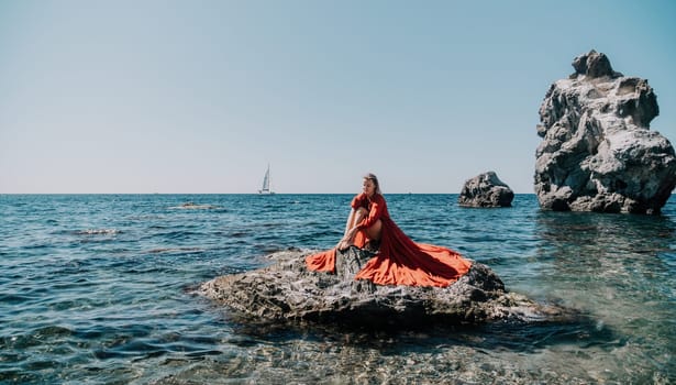 Woman travel sea. Young Happy woman in a long red dress posing on a beach near the sea on background of volcanic rocks, like in Iceland, sharing travel adventure journey