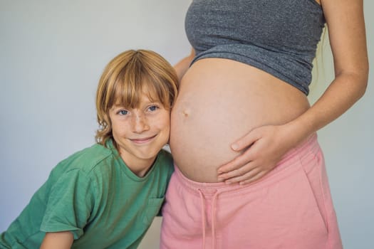 Young beautiful pregnant woman and eldest son. The cute boy leaned his ear against his mother's belly. Expecting a baby in the family concept. Preparing an older child for a younger one.