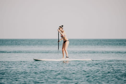 Sea woman sup. Silhouette of happy middle aged woman in rainbow bikini, surfing on SUP board, confident paddling through water surface. Idyllic sunset. Active lifestyle at sea or river