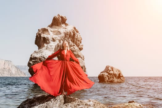 Woman travel sea. Young Happy woman in a long red dress posing on a beach near the sea on background of volcanic rocks, like in Iceland, sharing travel adventure journey