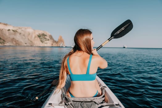 Woman in kayak back view. Happy young woman with long hair floating in transparent kayak on the crystal clear sea. Summer holiday vacation and cheerful female people relaxing having fun on the boat