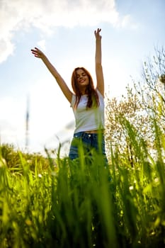 joyful slender woman posing in a field with her arms raised high. High quality photo