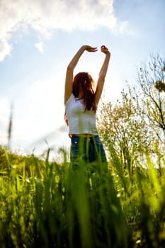 joyful slender woman posing in a field with her arms raised high. High quality photo