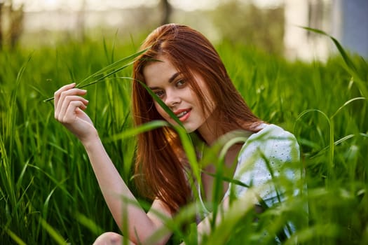 portrait of a cute red-haired woman sitting in tall grass and holding a leaf in her hands. High quality photo