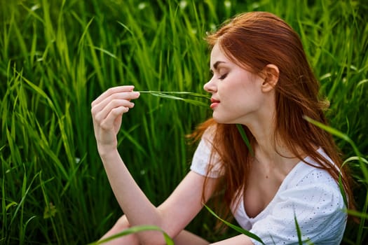 portrait of a beautiful redhead woman sitting in the grass on a sunny day at sunset. High quality photo