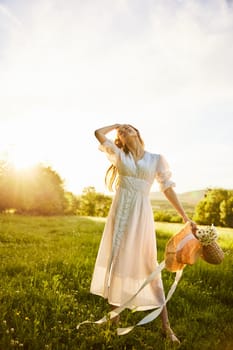 a beautiful woman in a light, summer dress stands in a chamomile field with a basket of flowers in her hands. High quality photo