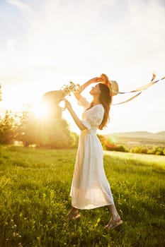 a woman in a white dress with a basket of daisies and a straw hat stands in a field during sunset in a light breeze. High quality photo