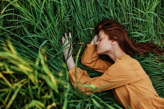 a close horizontal photo of a pleasant woman in a long orange dress resting lying in the tall grass with her eyes closed in sunny weather at sunset with her arms outstretched. Street photography,. High quality photo