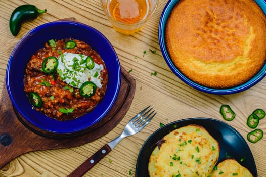 Black bean chili con carne in bowl with corn bread, potatoes. and beer. Tex-Mex style beef chili with sour cream, cilantro and jalapenos. Flat lay top down shot.