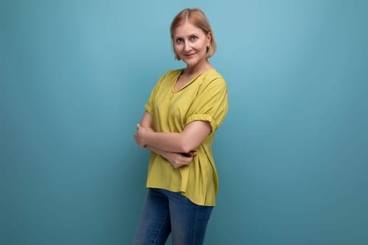 attractive 50s blonde woman in yellow t-shirt on blue background.