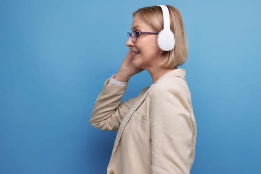 close-up portrait of a 50s middle-aged business woman in a jacket listening to music with headphones on a studio background with copy space.