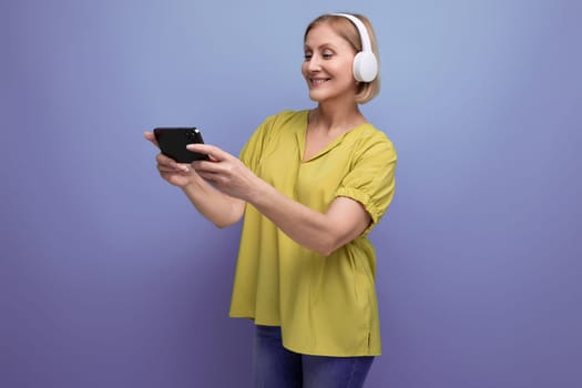 blonde 50s woman watching broadcast on smartphone using headphones.