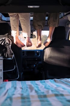 two unrecognizable women relaxing with feet dangling off the elevated bed of a camper van, concept of road trip adventure with best friend and van life relaxation, copy space for text