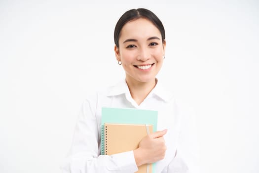Successful young asian woman, teacher with notebooks, looking confident and smiling, white studio background.