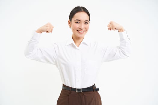 Business and corporate women. Strong and successful asian woman entrepreneur, shows biceps, flexing muscles, smiling pleased, white background.