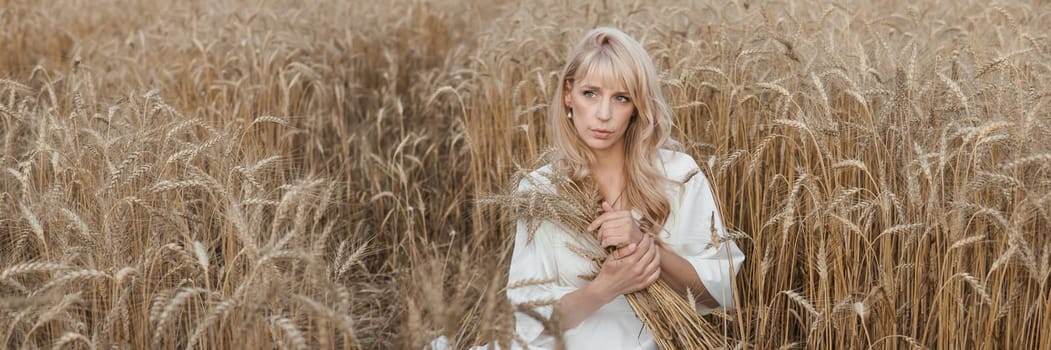 A blonde woman in a long white dress walks in a wheat field. The concept of a wedding and walking in nature.