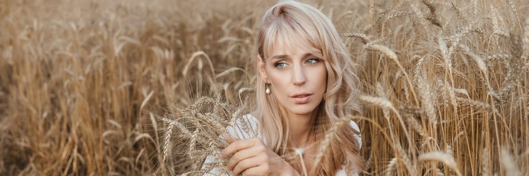 A blonde woman in a long white dress walks in a wheat field. The concept of a wedding and walking in nature.