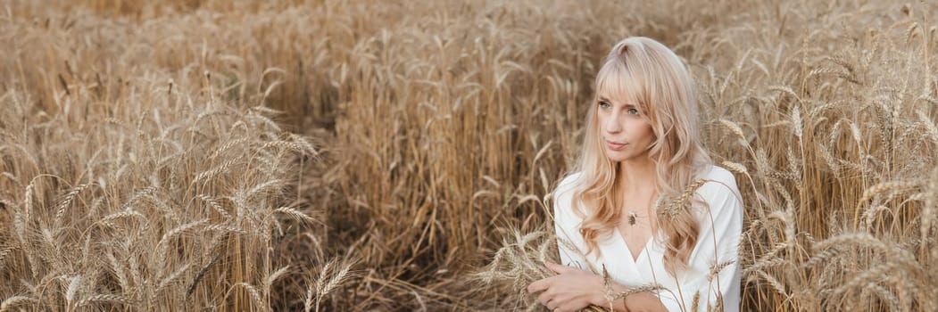 A blonde woman in a long white dress walks in a wheat field. The concept of a wedding and walking in nature.