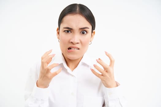 Angry office lady, asian businesswoman screams and clenches fists from anger, shakes from frustrated, stands over white background, loses temper.