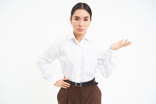 Confused lady boss, businesswoman shows open hand, shrugs shoulders with puzzled face, stands over white background.