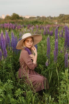 A beautiful woman in a straw hat walks in a field with purple flowers. A walk in nature in the lupin field.