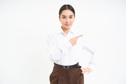 Business. Corporate asian woman points finger right, shows advertisement, banner promo, stands over white background.