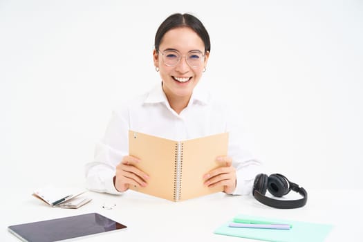 Image of hardworking student, asian woman in glasses studying, holding notebook, working on project, isolated over white background.
