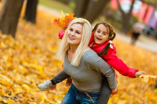 Young mother playing with her daughter in autumn park.