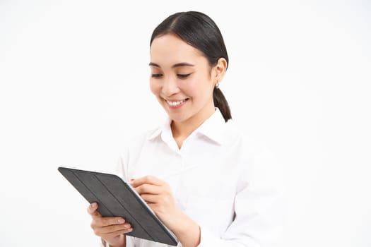 Portrait of businesswoman working on digital tablet, creating diagrams for meeting conference on gadget, standing over white background.