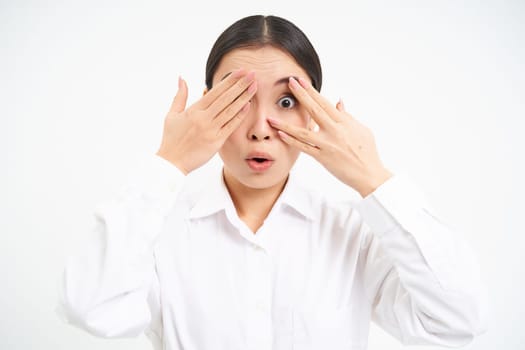 Asian woman entrepreneur, businesswoman shuts her eyes with hands, stands blindfolded against white studio background.