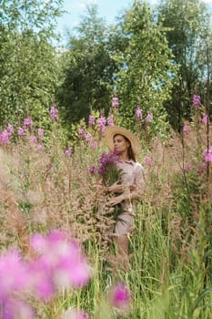 A young woman in nature with a bouquet of pink wild flowers. A bouquet of Ivan-tea in the hands of a woman.