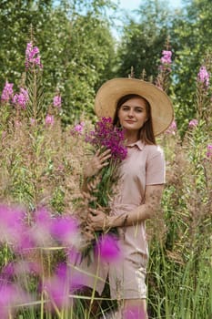 A young woman in nature with a bouquet of pink wild flowers. A bouquet of Ivan-tea in the hands of a woman.