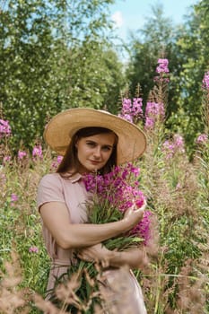 A young woman in nature with a bouquet of pink wild flowers. A bouquet of Ivan-tea in the hands of a woman.