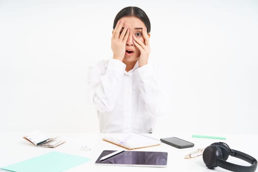 Image of asian office lady shuts her eyes embarrassed, sees something scary, sits at workplace, white background.