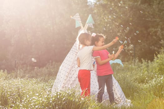 childhood and hygge concept - happy little girls playing in kids tent.