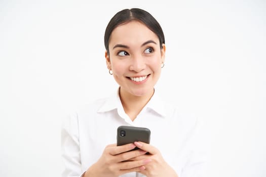 Image of asian saleswoman, office manager holding smartphone, working on text for social media, using cellphone, white background.