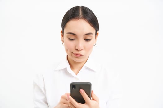 Portrait of korean businesswoman with worried face, reading message on mobile phone screen, isolated on white.