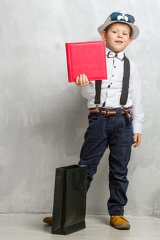 Back to school. Funny little boy in glasses pointing up on blackboard. Child from elementary school with book and bag. Education. Kid with a book