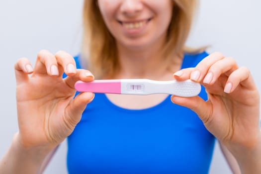 Smiling woman in blue holding a positive pregnancy test.