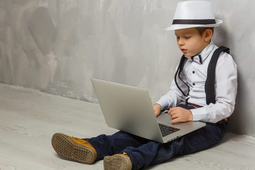 Little boy using laptop against grey wall background