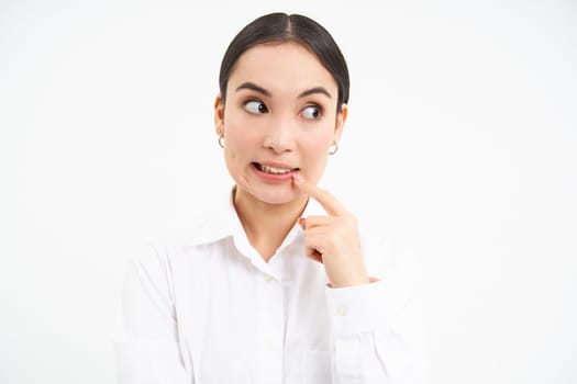 Office and business concept. Young worried asian female manager, bites her finger and looks complicated, stands over white background.